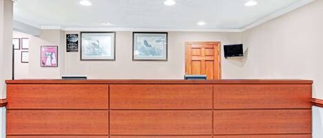 A reception area with a wooden counter, framed artwork on the wall, and a television mounted above it.