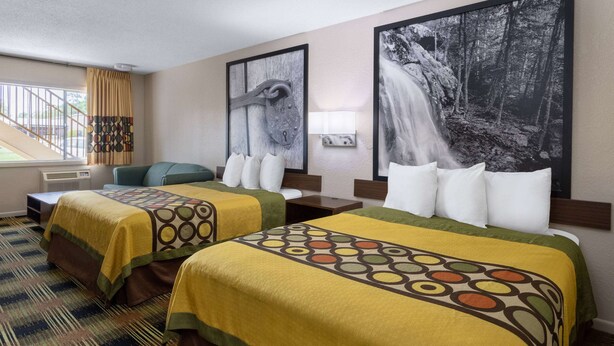 Habitación de hotel con dos camas, un sofá y un ventanal grande con cortinas.