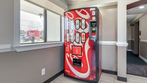 A vending machine with a Coca-Cola logo, located in a hallway with a window and an elevator. - Red Roof Inn Suffolk (Suffolk)