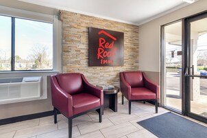 Zona de recepción de Red Roof Inn con dos sillones de cuero, una pared de piedra y un ventanal grande.
