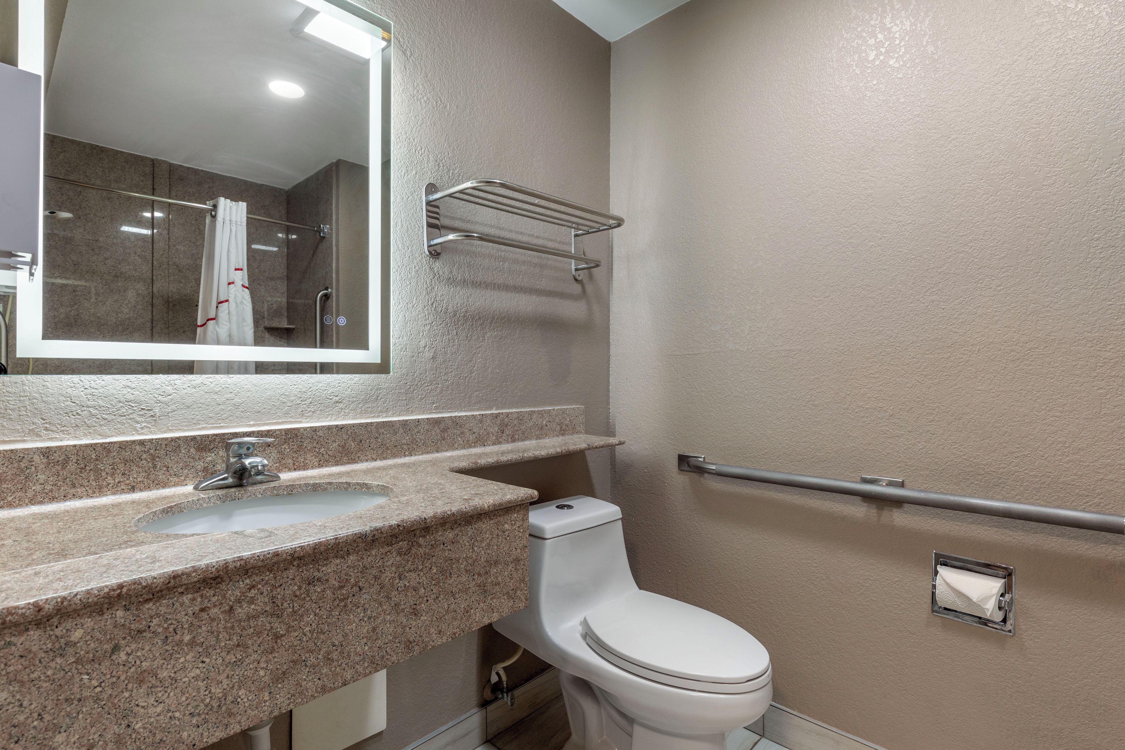 A bathroom with a granite countertop, a white toilet, a mirror, and a towel rack.