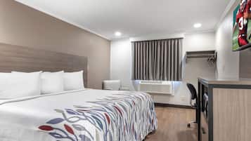 Hotellihuone, jossa on suuri sänky, työpöytä, tuoli, televisio ja ikkuna, jossa on verhot.