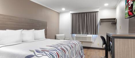 Habitación de hotel con una cama grande, un escritorio, una silla, un televisor y una ventana con cortinas.