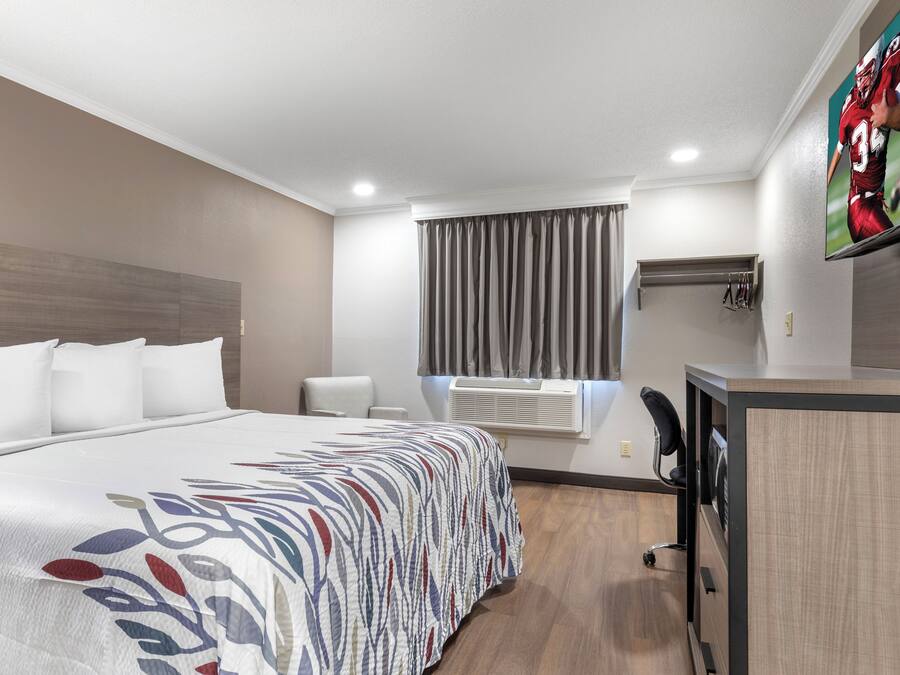 A hotel room with a large bed, a desk, a chair, a television, and a window with curtains.