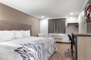 Habitación de hotel con una cama grande, un escritorio, una silla, un televisor y una ventana con cortinas.