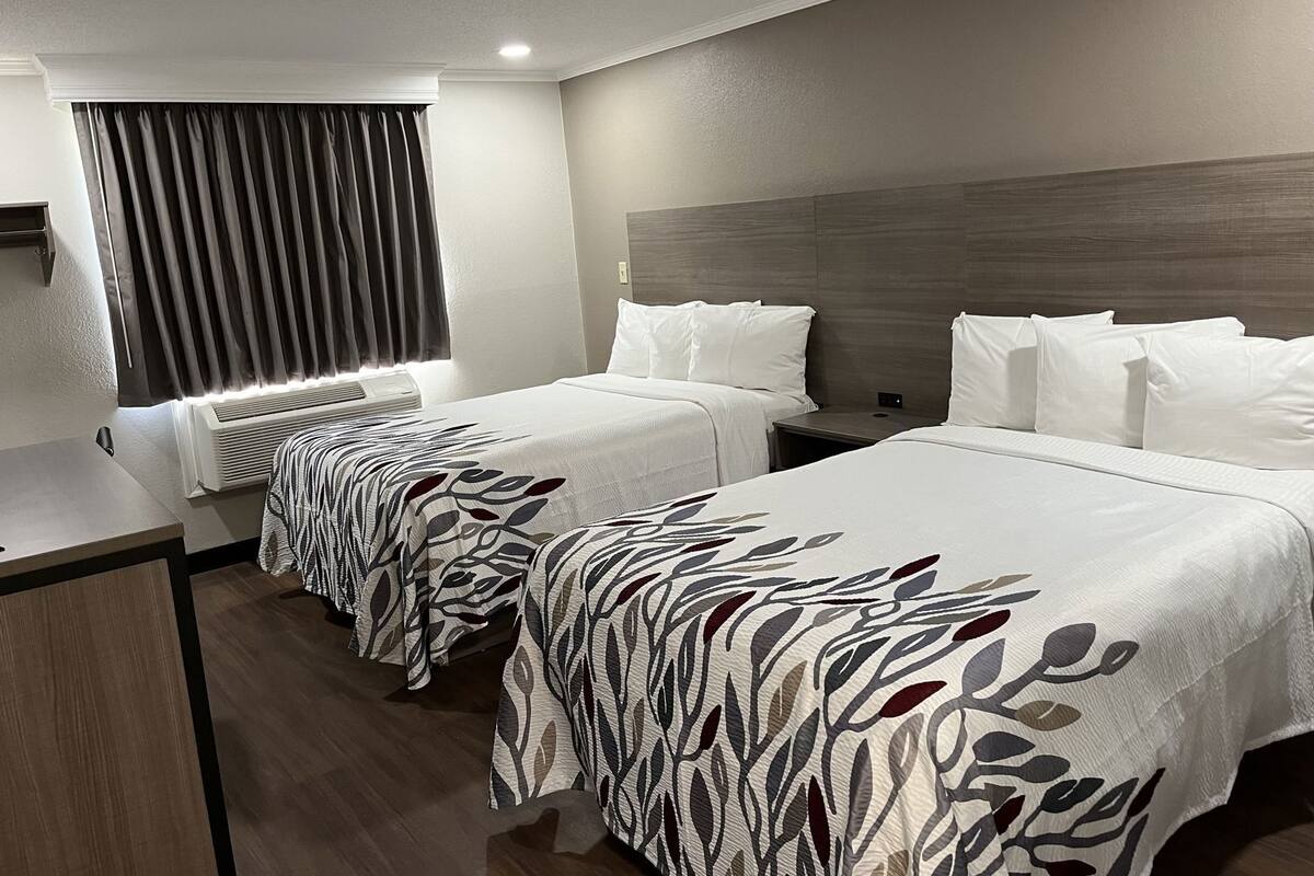 Een hotelkamer met twee bedden, een bureau en een raam met gordijnen.