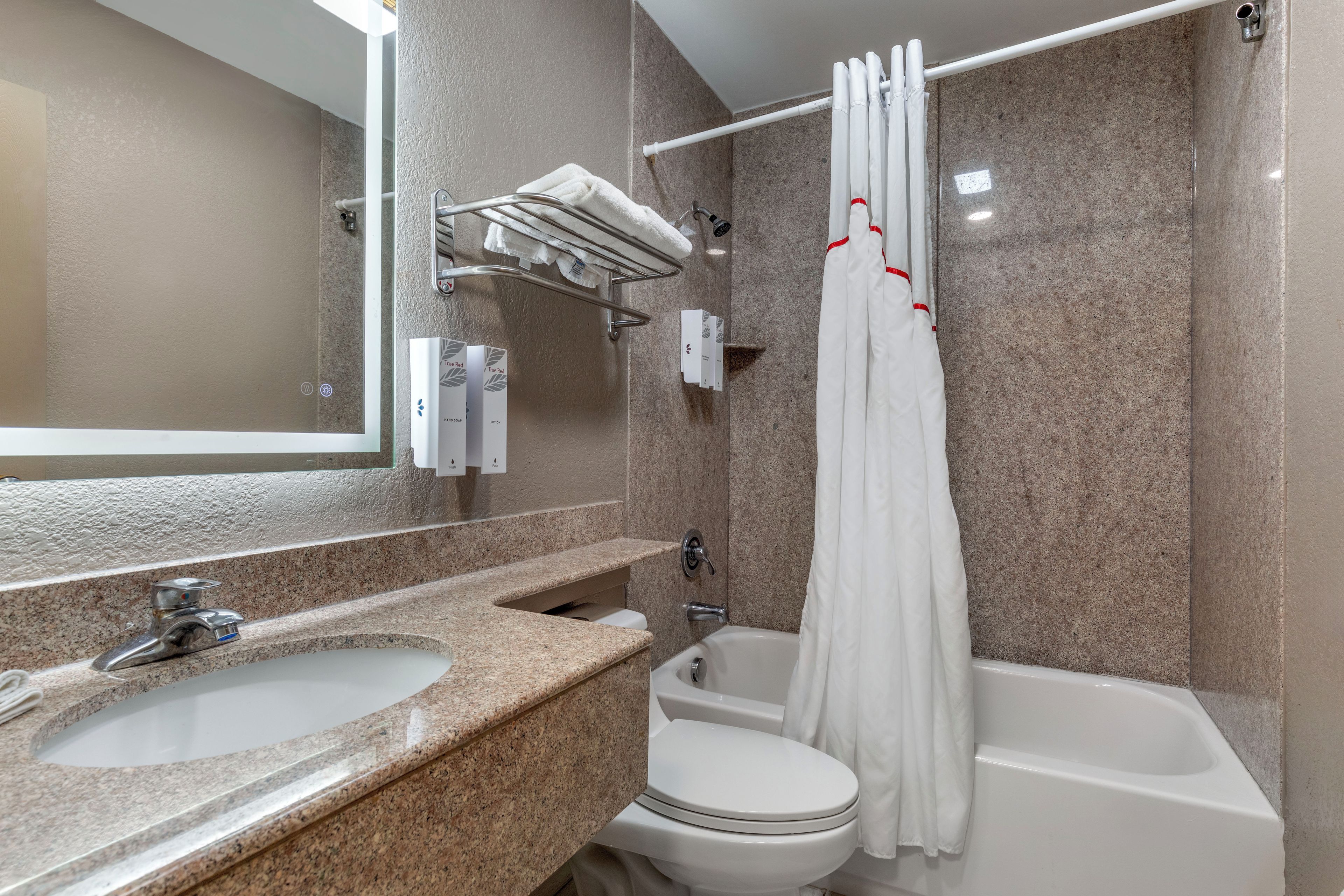 A bathroom with a granite countertop sink, a toilet, and a bathtub with a shower curtain.