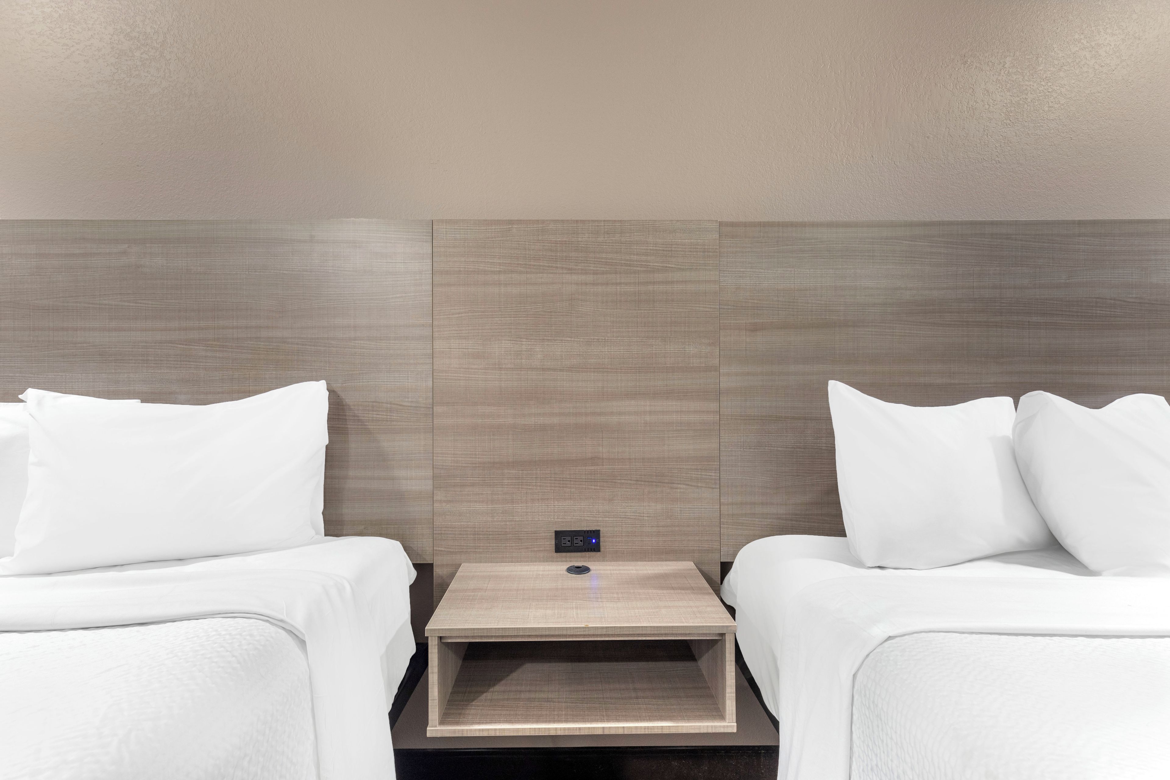 Une chambre d’hôtel avec deux lits, une table de chevet et un panneau de commande fixé au mur.