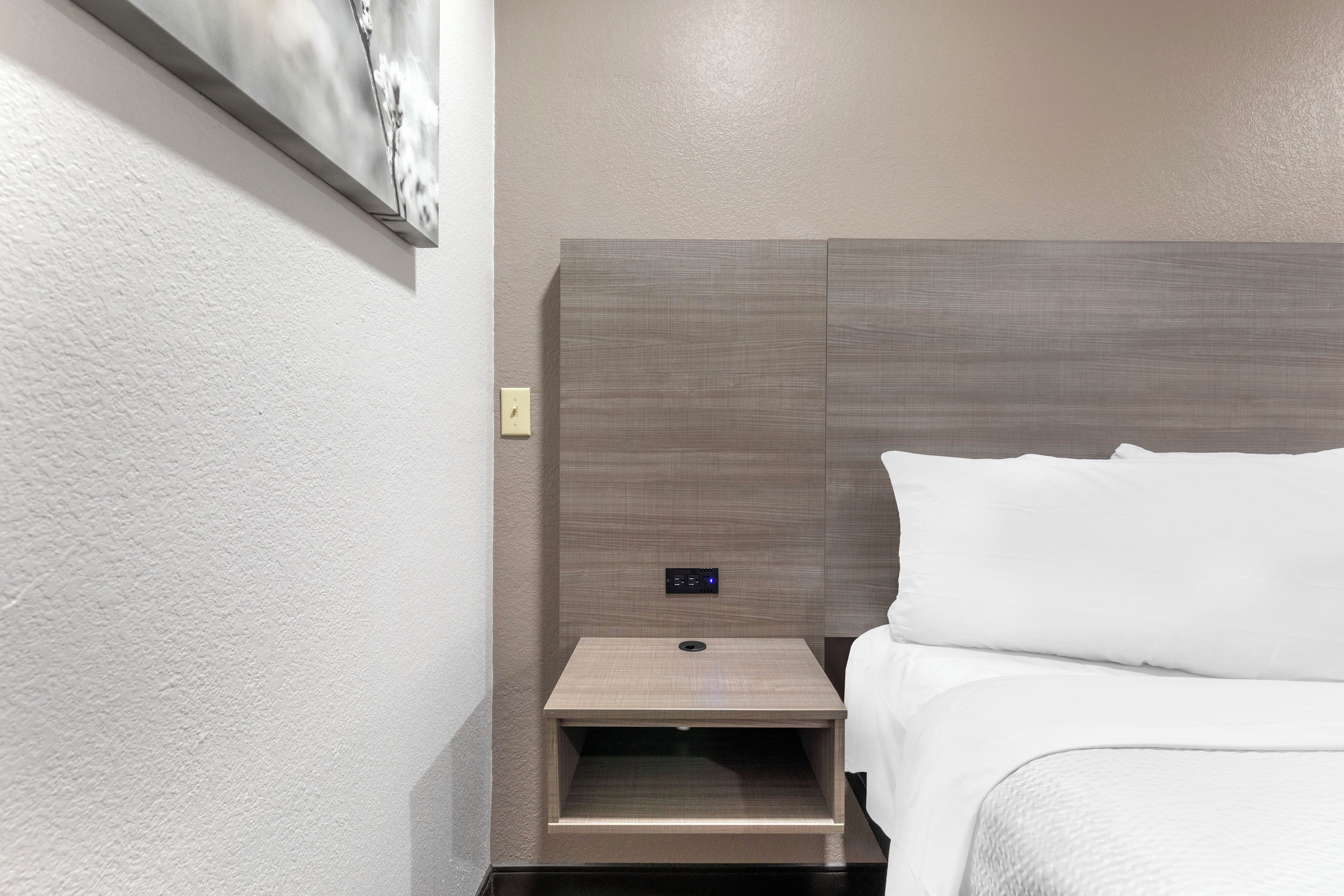 A hotel room with a bed, a nightstand, and a wall-mounted control panel.
