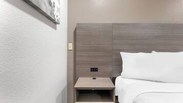 A hotel room with a bed, a nightstand, and a wall-mounted control panel.