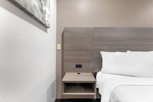 A hotel room with a bed, a nightstand, and a wall-mounted control panel.