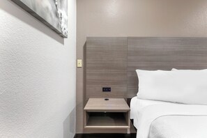 A hotel room with a bed, a nightstand, and a wall-mounted control panel.