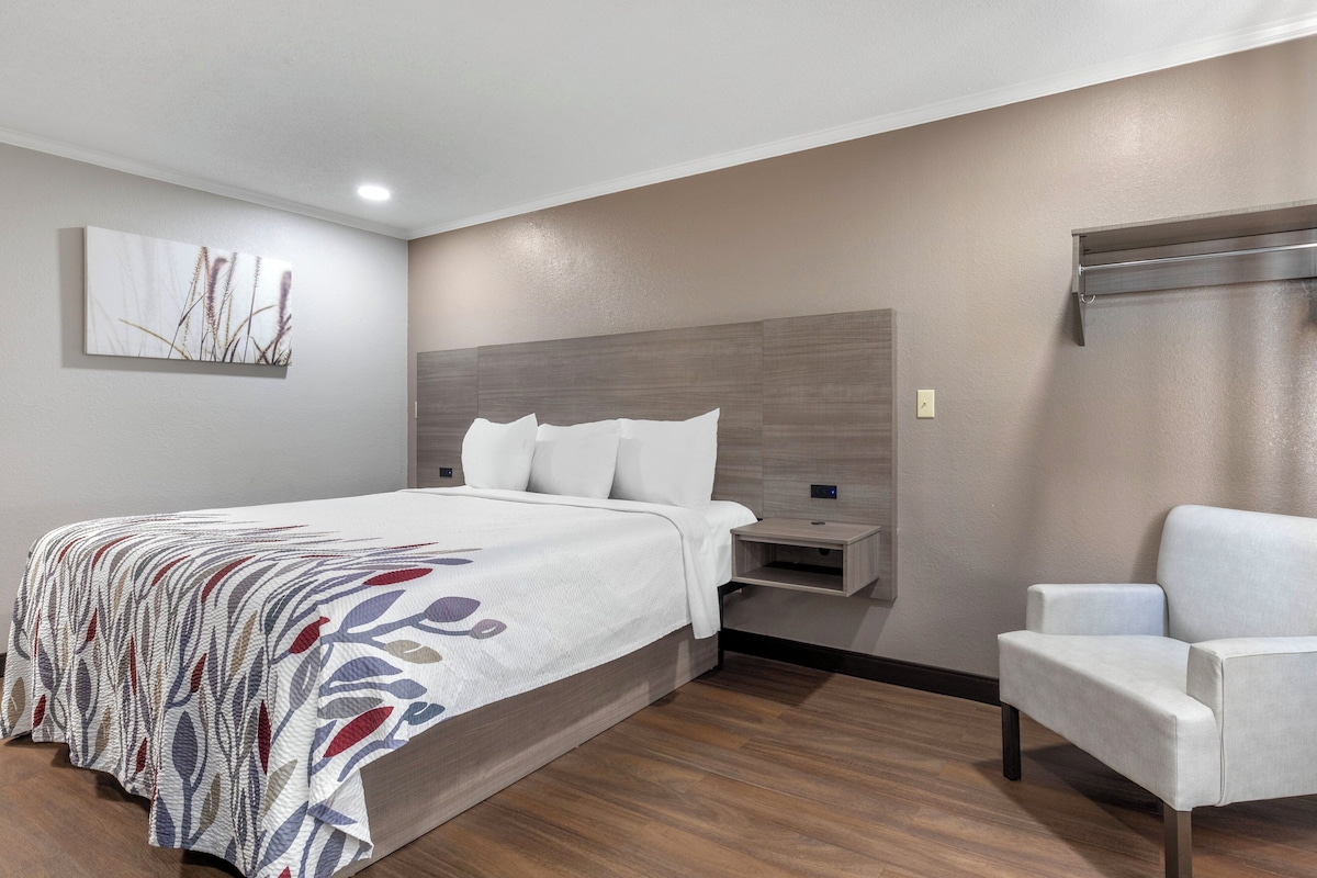 Une chambre d’hôtel moderne, dotée d’un grand lit, d’une table de chevet, d’une chaise et d’un téléviseur fixé au mur.