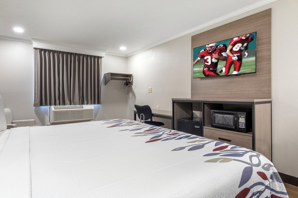 Une chambre d’hôtel dotée d’un grand lit, d’un téléviseur à écran plat fixé au mur, d’un bureau avec une chaise, d’un four à micro-ondes et d’un petit placard.