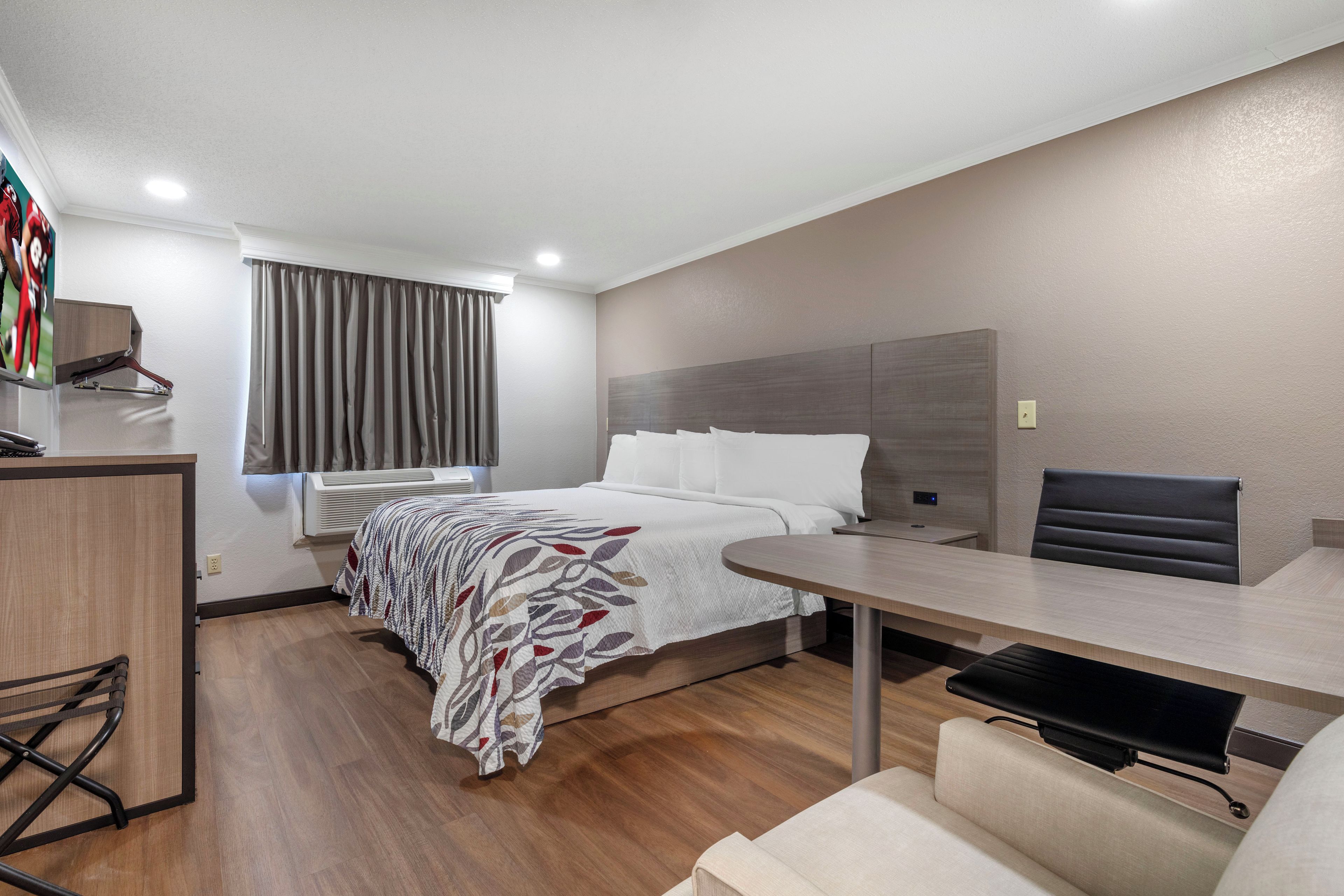 A hotel room with a bed, a desk, a chair, a wardrobe, and a window with curtains.