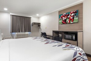 Een hotelkamer met een bed, een wandtelevisie, een bureau met stoel, een magnetron en een airconditioner.