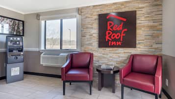 Red Roof Inn -hotellin aula, jossa on kaksi nahkaista nojatuolia, pankkiautomaatti ja kiviseinä.