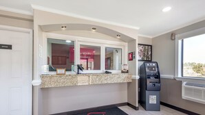 A reception area with a counter, a phone, an ATM, and a door labeled 'OFFICE'. - Red Roof Inn Suffolk (Suffolk)