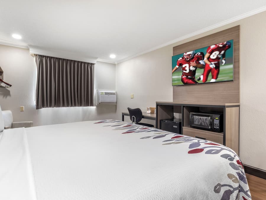 Habitació d'hotel amb un llit gran, escriptori, televisió i finestra amb cortines.