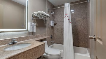 A bathroom with a granite countertop, a white toilet, a bathtub, and a shower curtain.