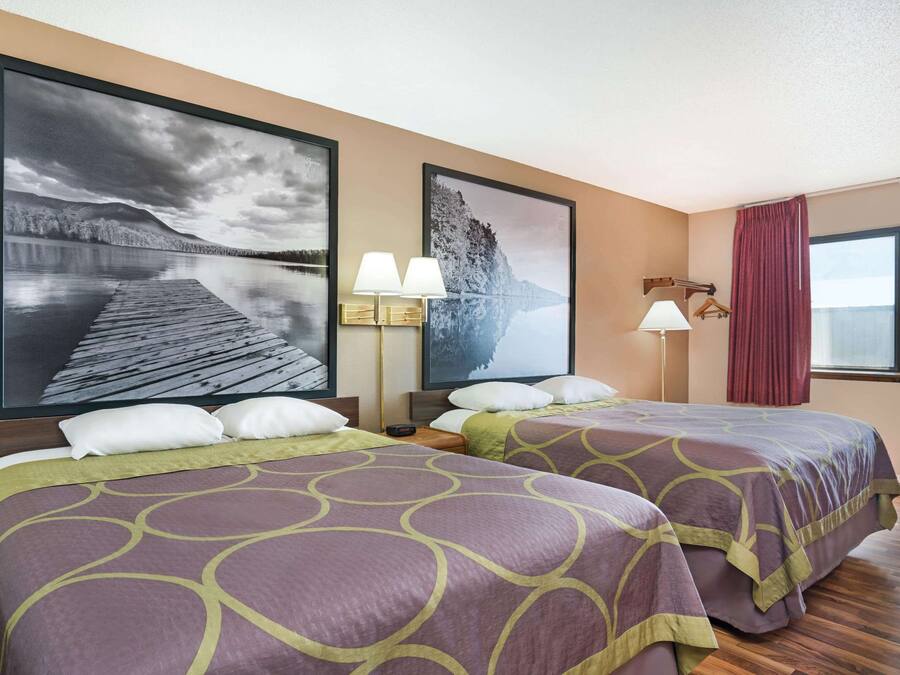 A hotel room with two beds, a large window, and two wall-mounted lamps.