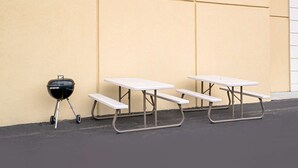 Una mesa de picnic frente a una pared color crema, con una parrilla negra cerca.