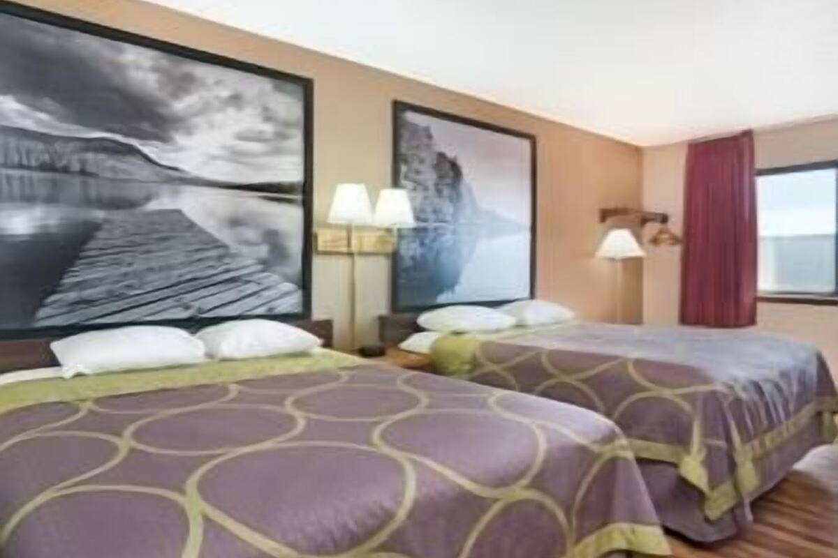 Ein Hotelzimmer mit zwei Betten, einem großen Meeresblick-Gemälde, einem Fenster mit Aussicht und einer Lampe auf dem Nachttisch.