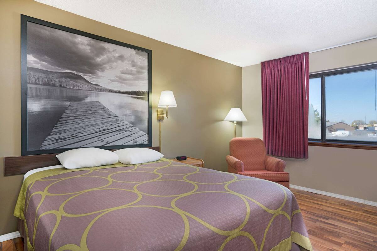 Ein Hotelzimmer mit einem großen Bett, zwei Wandlampen, einem Sessel und einem großen Fenster mit Vorhängen.