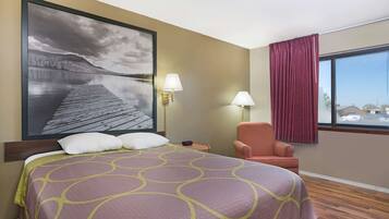 Una habitación de hotel con una cama grande, dos lámparas de pared, una silla y un ventanal con cortinas.