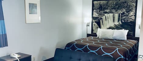 Una habitación de hotel moderna con una cama grande, un sofá, una mesa de centro de madera, una mesita de noche con teléfono y una lámpara de pared.