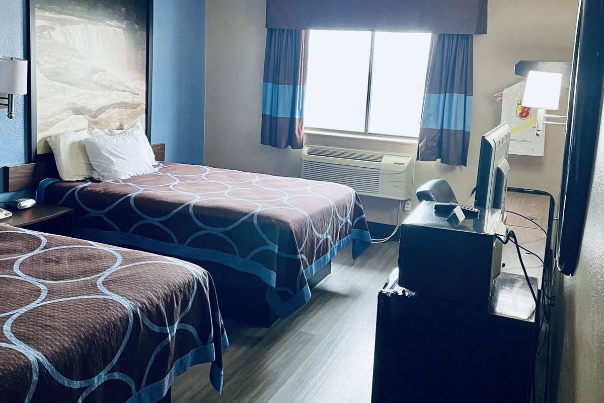 Habitación de hotel con dos camas, un escritorio, una silla, un televisor y una ventana con cortinas.