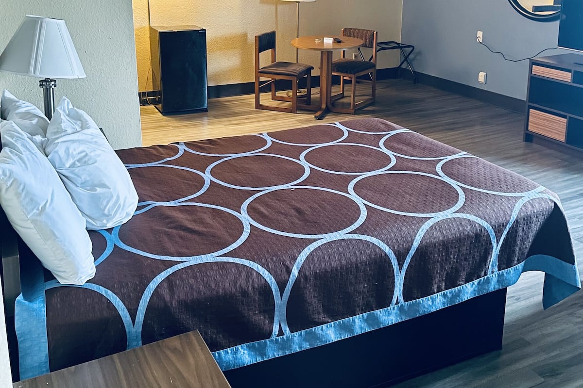 Habitación de hotel con cama, escritorio, silla, lámpara, espejo y altavoz.