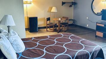 A hotel room with a bed, a desk, a chair, a lamp, a mirror, and a speaker.
