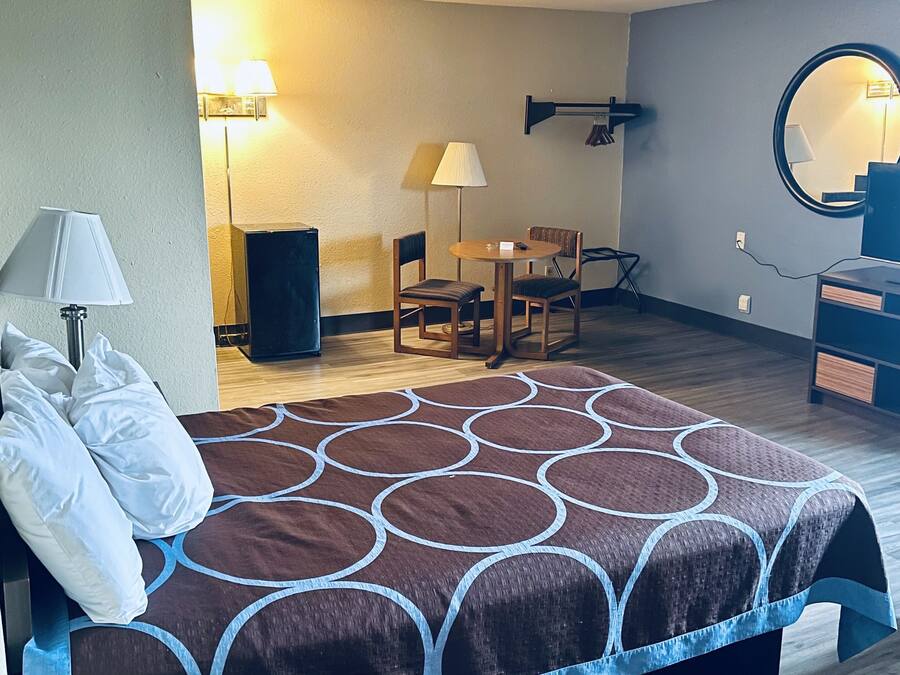 A hotel room with a bed, a desk, a chair, a lamp, a mirror, and a speaker.