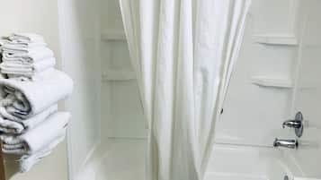 Et badeværelse med badekar, toilet og vask. Der er håndklæder stablet på en hylde og en badeforhæng.