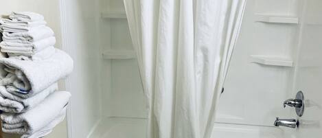 A bathroom with a bathtub, toilet, and sink. There are towels stacked on a shelf and a shower curtain.