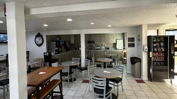 Interior de restaurante con varias mesas y sillas, un reloj en la pared y una máquina expendedora.