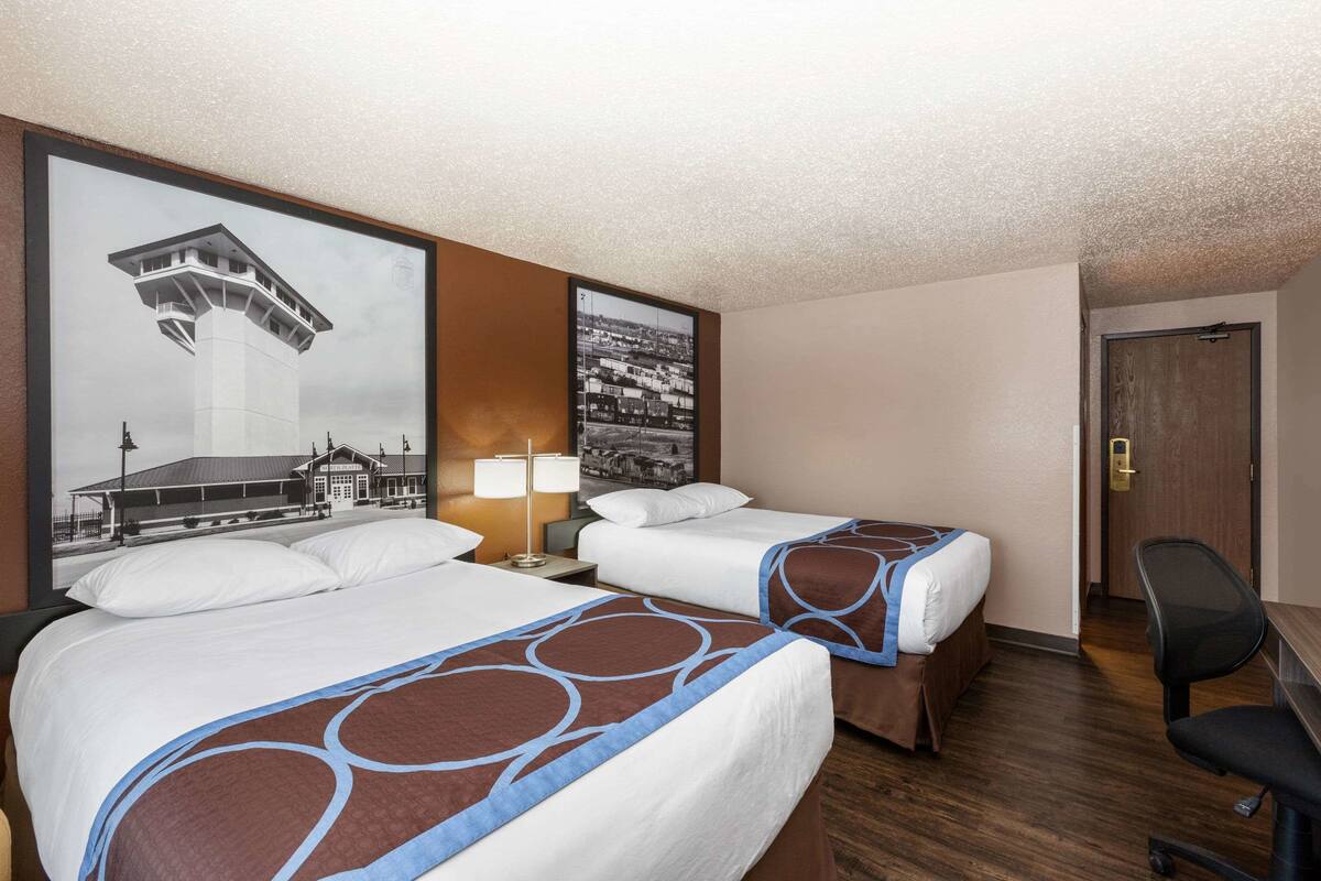 A hotel room with two beds, a desk, and a chair. There are two framed pictures on the wall.