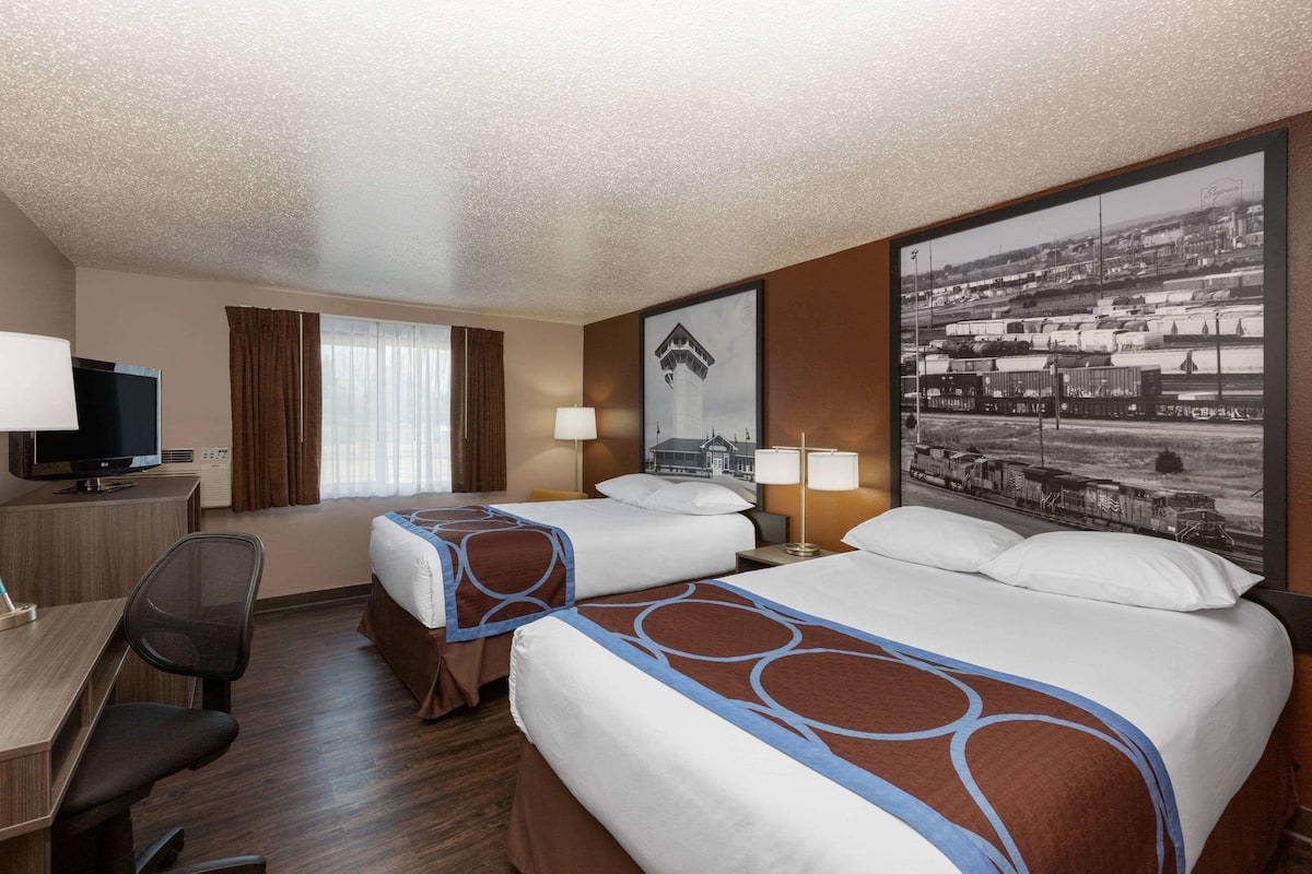 A hotel room with two beds, a desk, a chair, a TV, and a large cityscape picture on the wall.