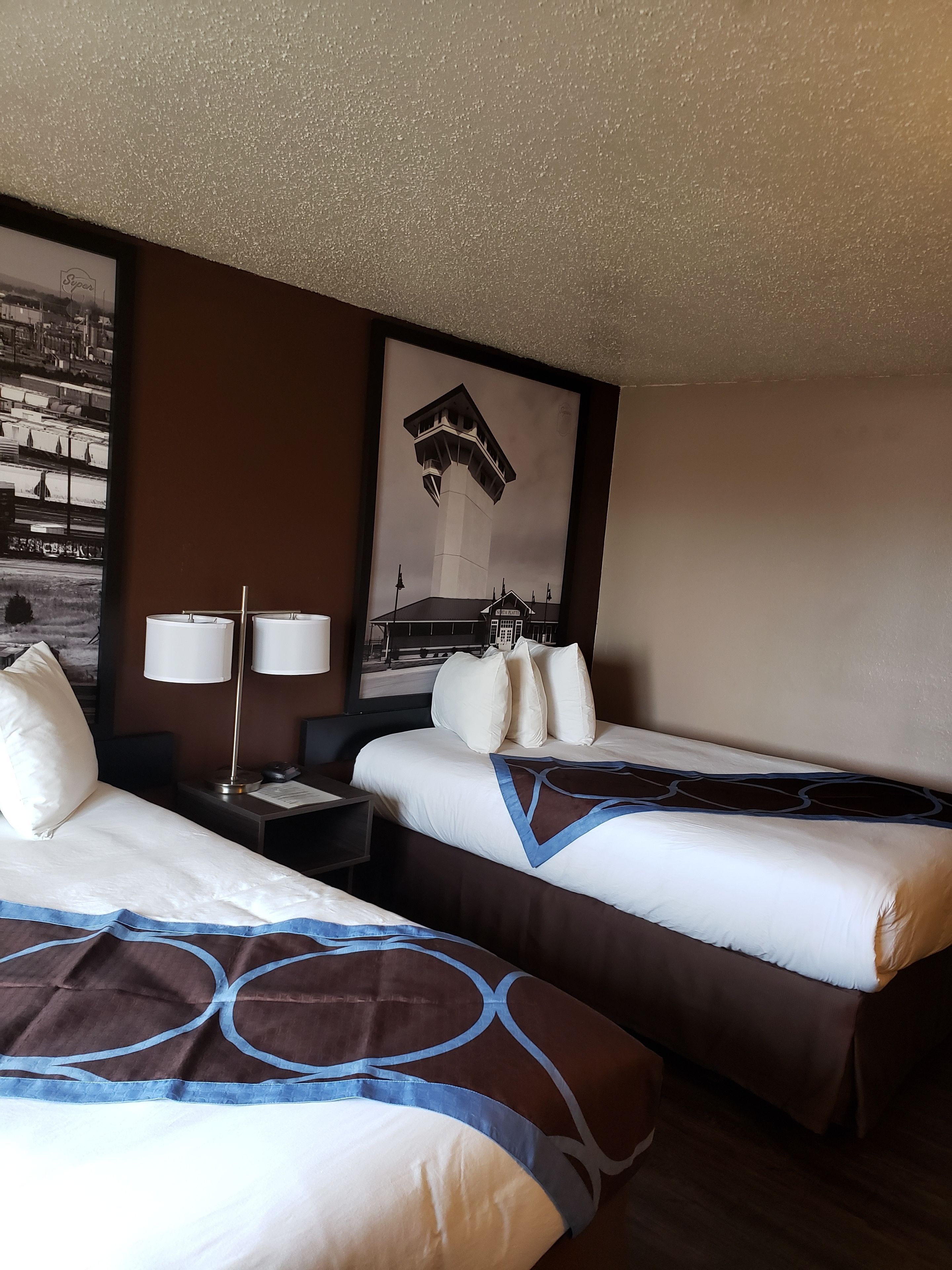 Une chambre d’hôtel avec deux lits, une table de chevet, une lampe et un tableau encadré au mur.