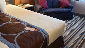 A hotel room with a large bed, a sofa, two lamps, and a striped carpet.