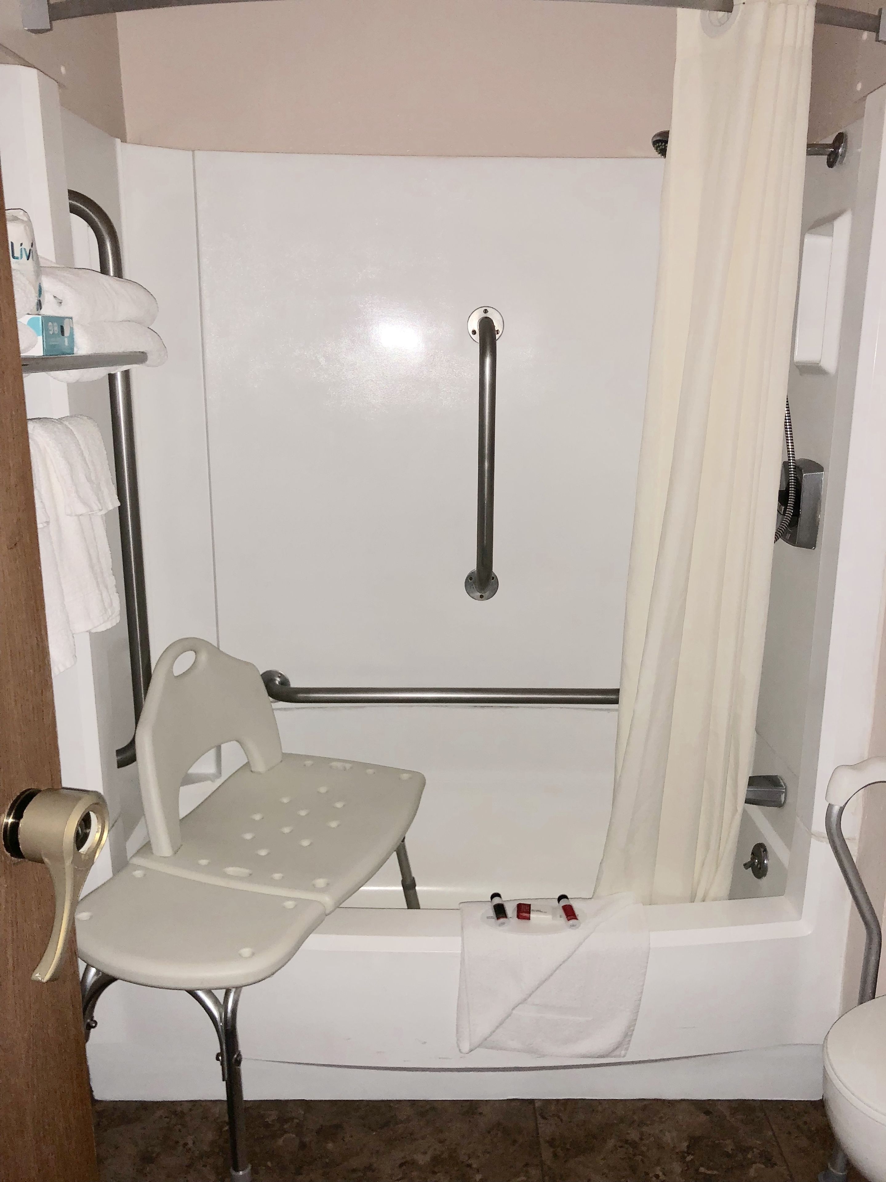 Un baño con ducha, barra de apoyo, silla y toallero.