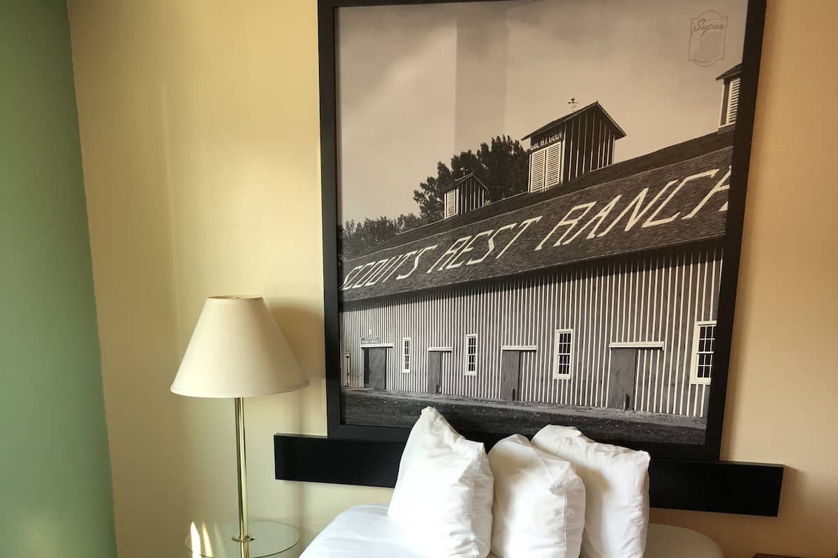 A hotel room with a bed, a framed picture on the wall, a lamp, and a nightstand.
