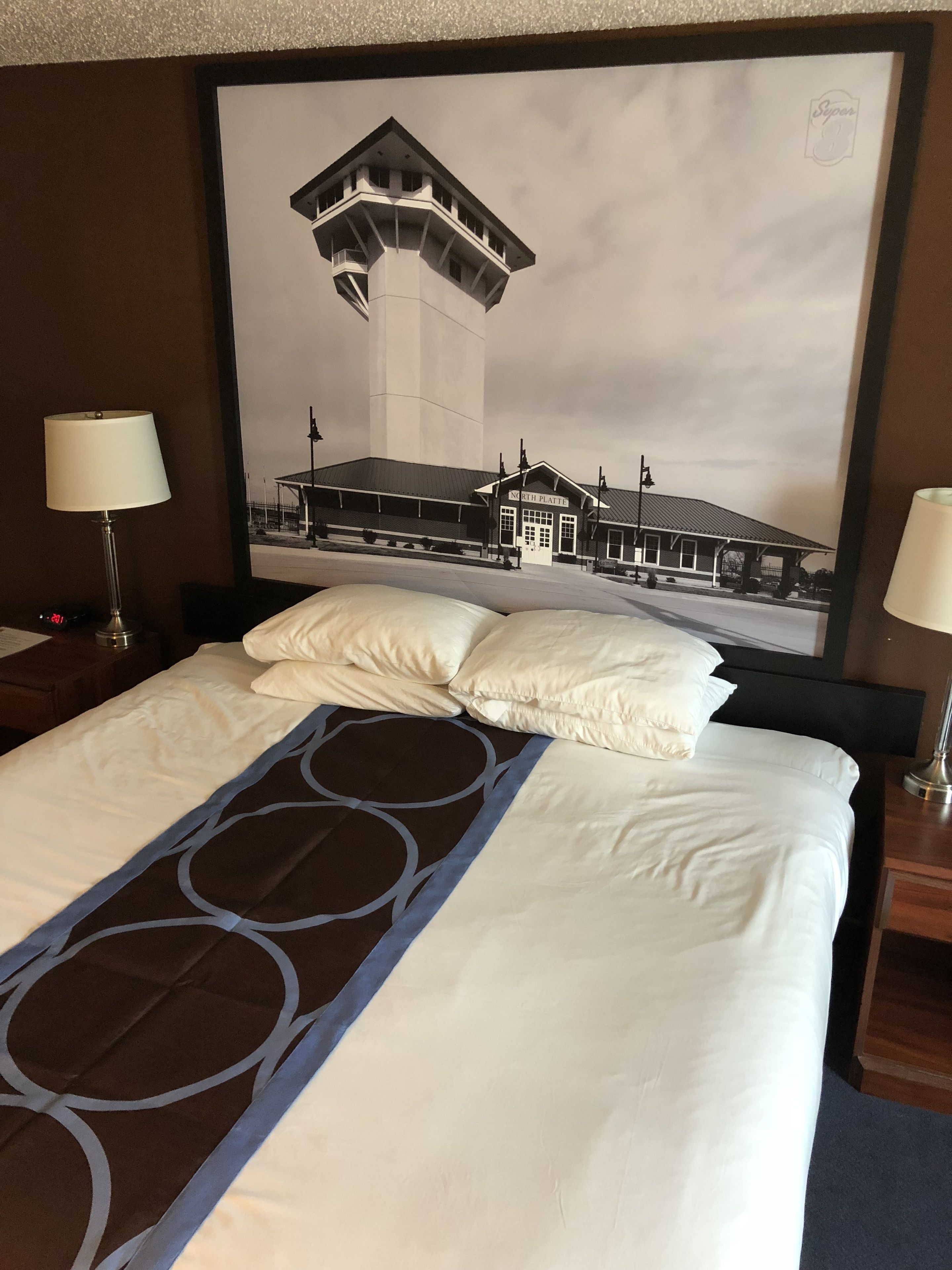 Une chambre d’hôtel avec un lit, deux lampes de chevet, un grand tableau encadré représentant un bâtiment et une couvre-lit bleue à motifs.