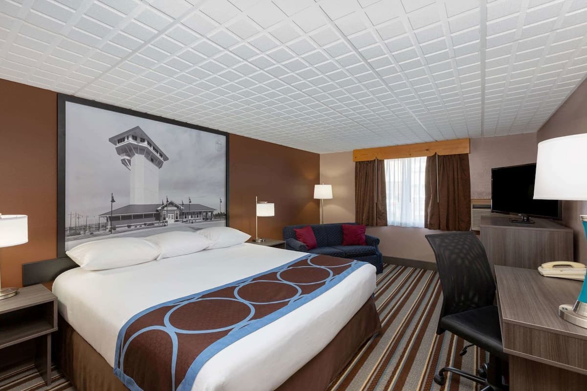 A hotel room with a large bed, a desk, a chair, a television, and a wall-mounted lamp.