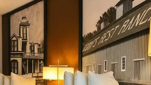 Habitación de hotel con una cama grande, varios almohadones, una mesita de noche con lámpara y un mural en la pared que representa un edificio.