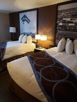 Habitación de hotel con dos camas, una mesita de noche con lámpara y un cuadro grande en la pared.