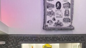 Zona de recepción de hotel con un cartel de Super 8, pared de azulejos y un mostrador de recepción con dos monitores.