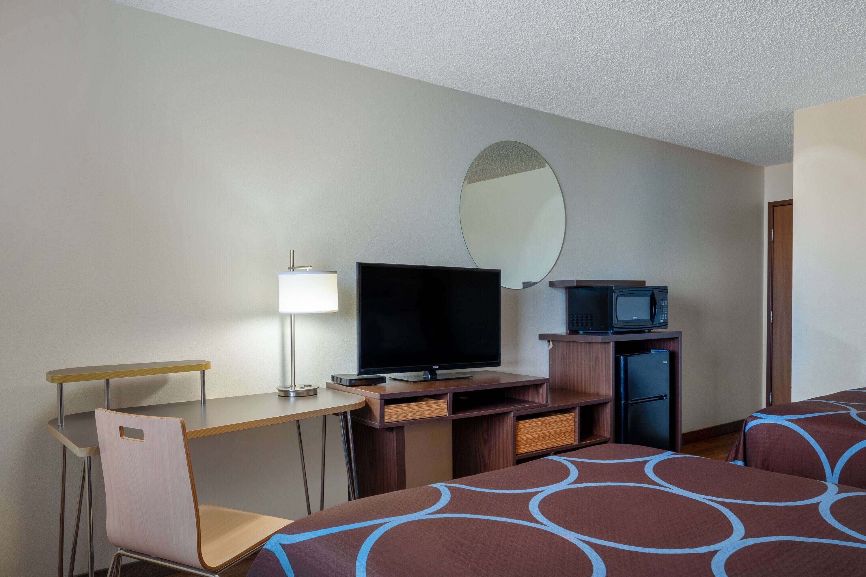 Ein Hotelzimmer mit Schreibtisch, Fernseher, Mikrowelle, Kühlschrank und zwei Betten mit gemusterten Bettbezügen.