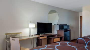 Ein Hotelzimmer mit Schreibtisch, Fernseher, Mikrowelle, Kühlschrank und zwei Betten mit gemusterten Bettbezügen.